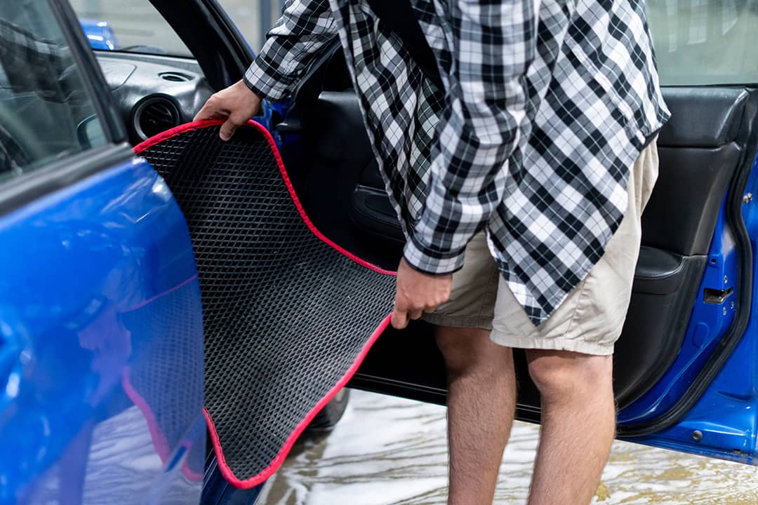 Man taking out dirty mat from car interior.
